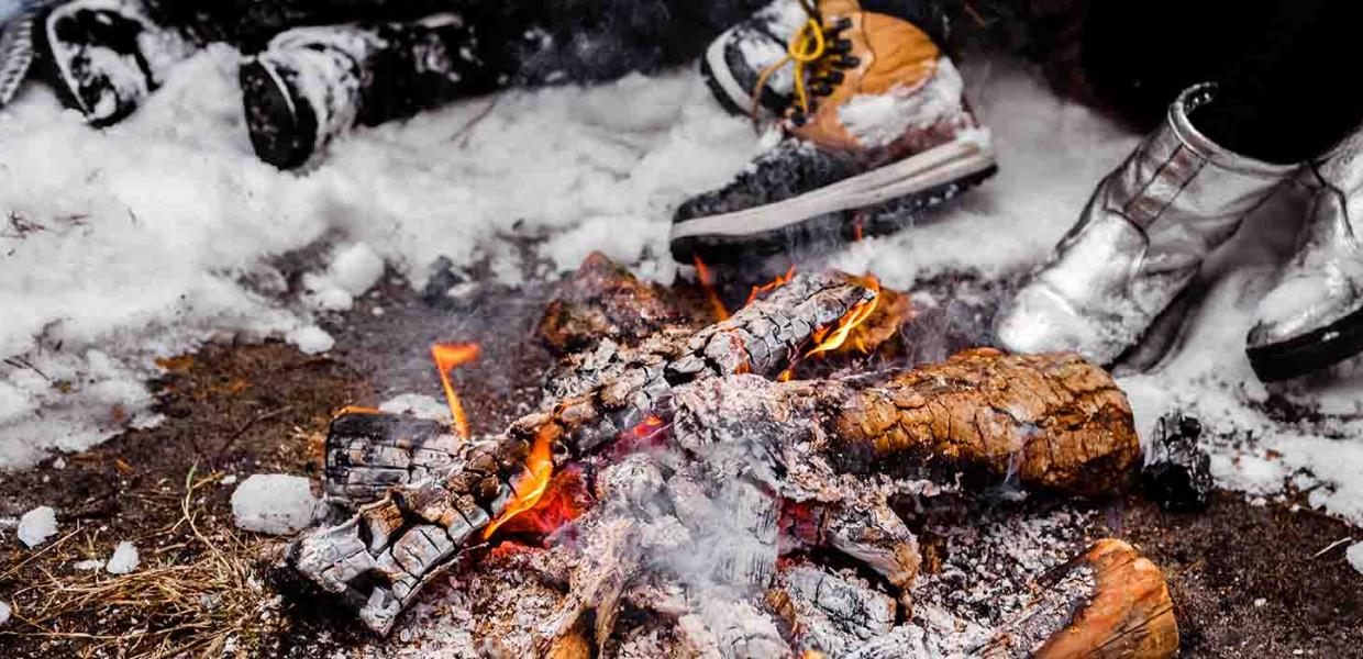 Folk sidder med store støvler ved det tændte bål en snefyldt vinter