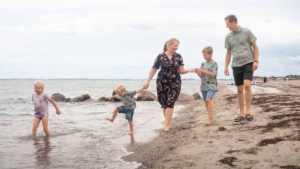 Familie går tur på Hasmark Strand og leger i vandet