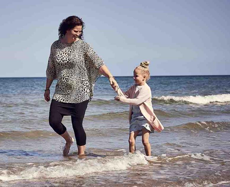 Mor og barn går i vandkanten på stranden ved Flyvesandet