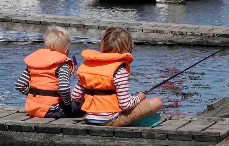 Børn iført orange sikkerhedsveste fisker fra en bådebro