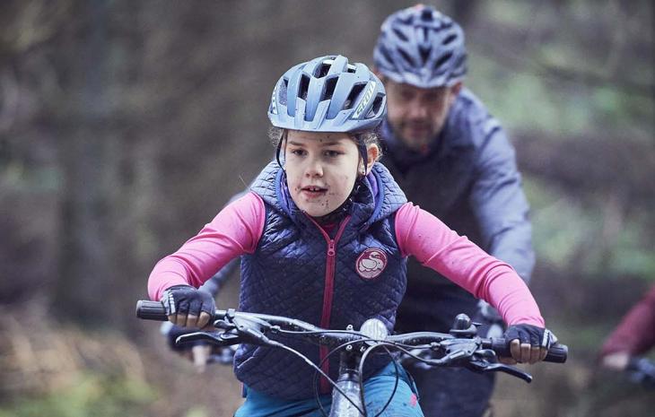 Familie med pige i forgrunden cykler på MTB i Langesø-skoven i efteråret